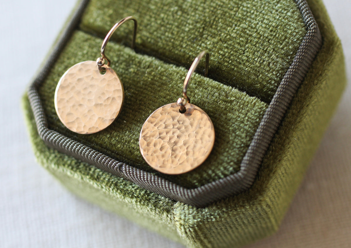 A pair of hammered round gold-tone drop earrings displayed in an olive green velvet jewelry box.